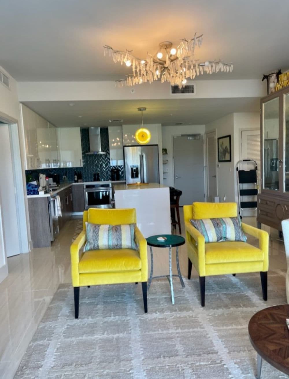 Bright modern apartment interior with yellow chairs, chandelier, and a stylish kitchen.