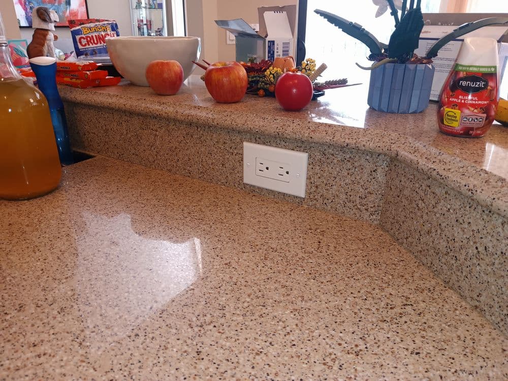 Kitchen countertop with apples, a bowl, decorative items, and a power outlet.