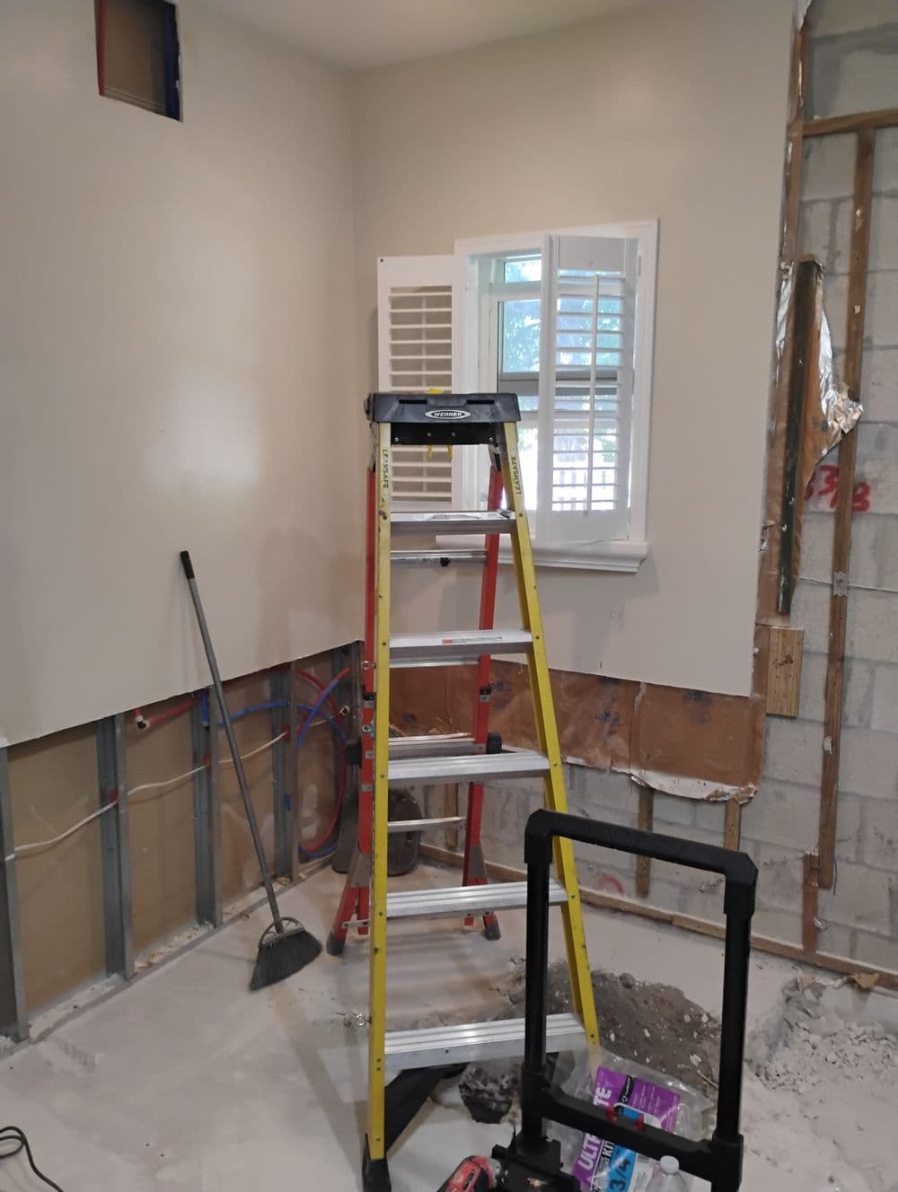 Room under construction with a ladder, exposed walls, and a window with shutters.