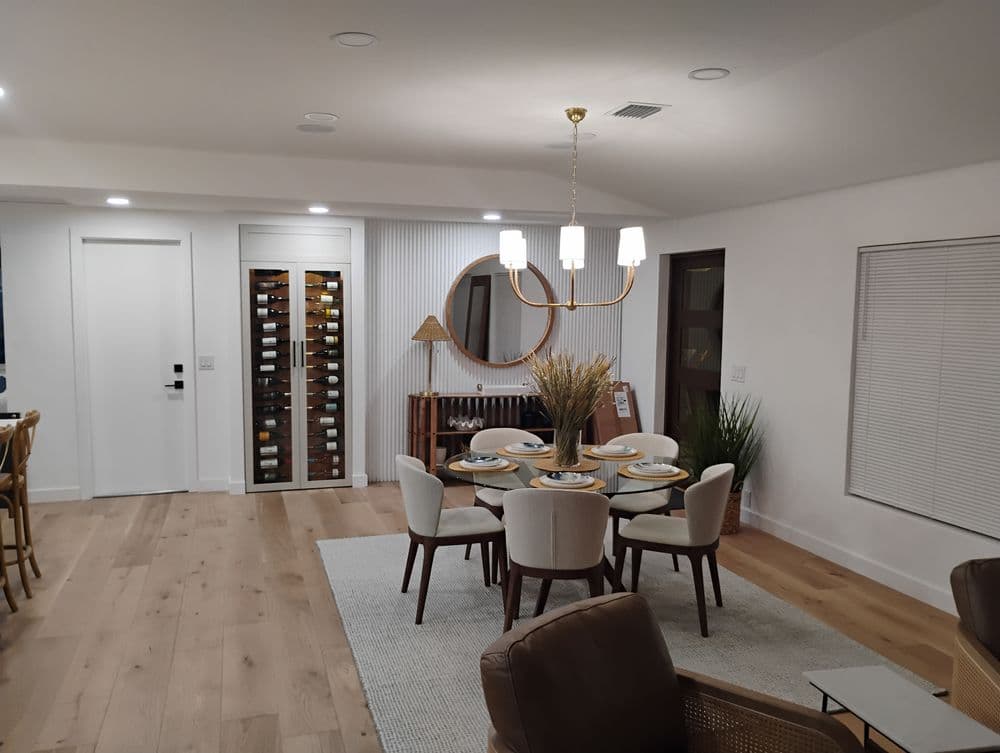 Modern dining room featuring a round table, stylish chairs, wine cellar, and decorative mirror.