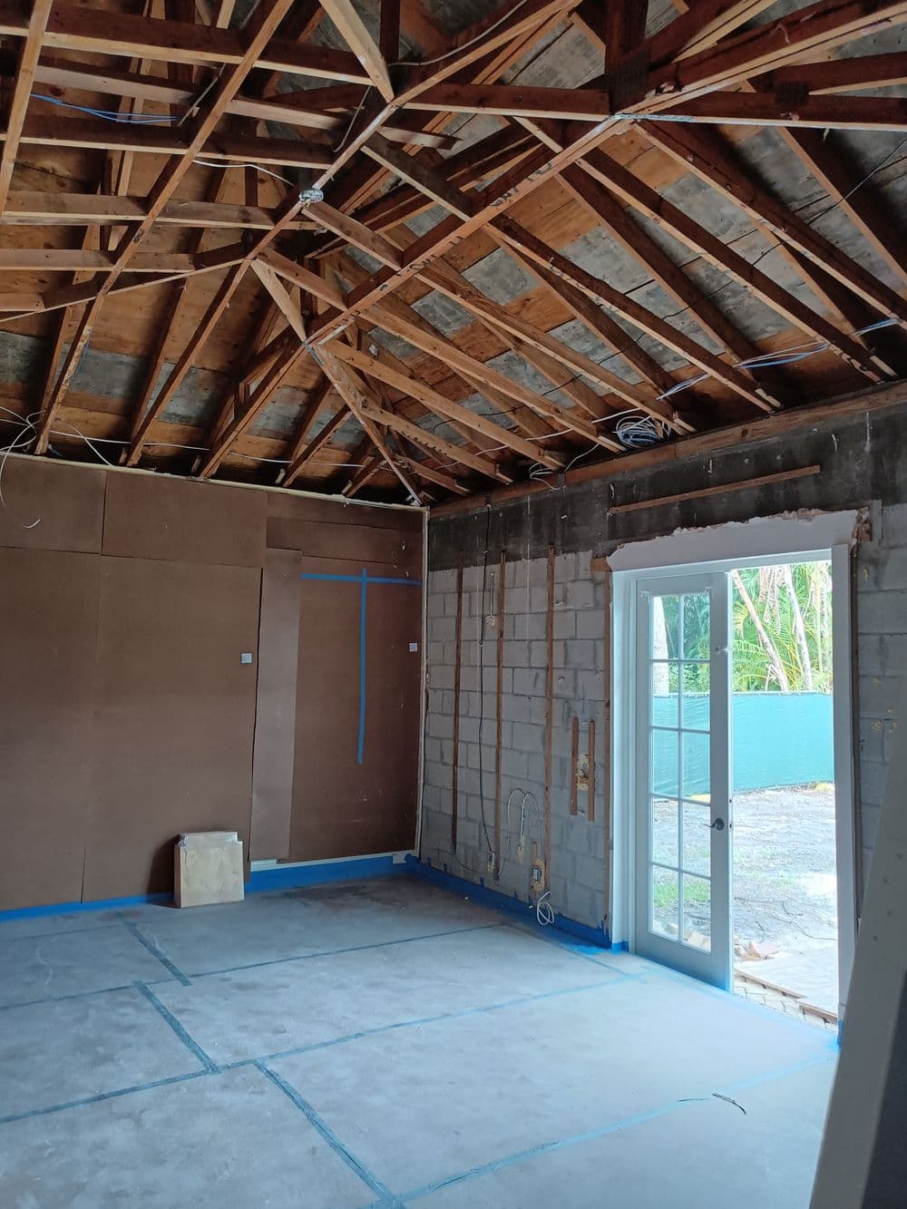 Interior of a room under renovation, featuring exposed rafters and blue tape markings.