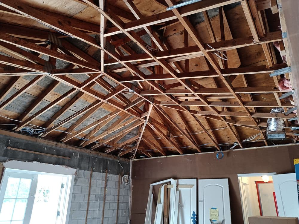 Exposed wooden beams and rafters in an unfinished room renovation. Construction materials visible.