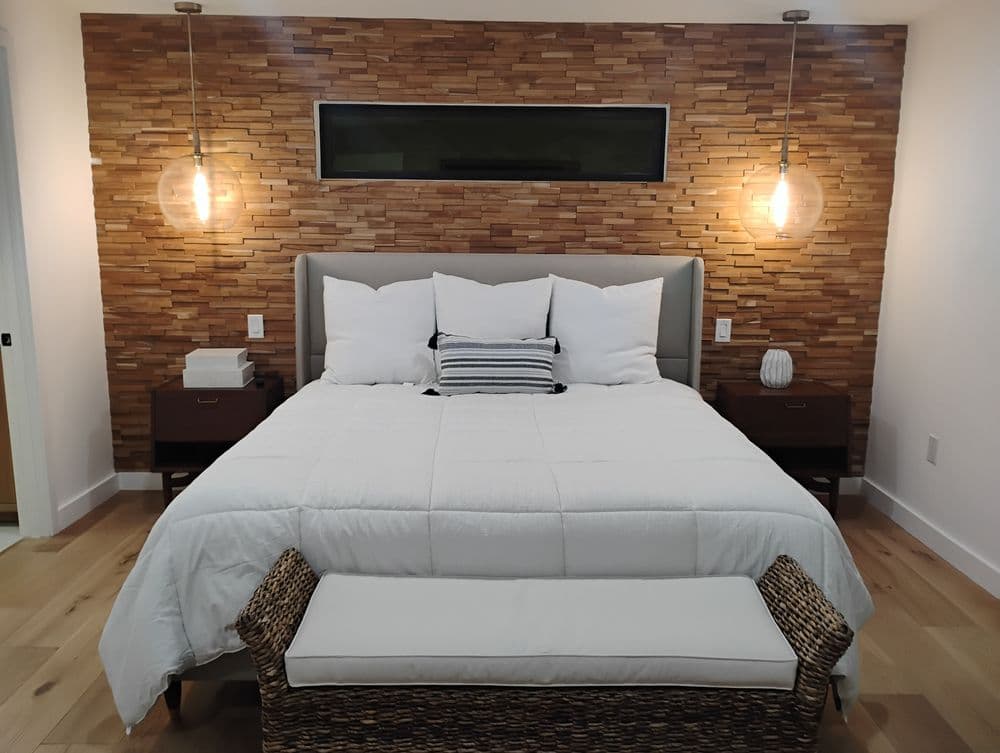 Modern bedroom featuring a stylish bed with white pillows, wooden accent wall, and pendant lights.